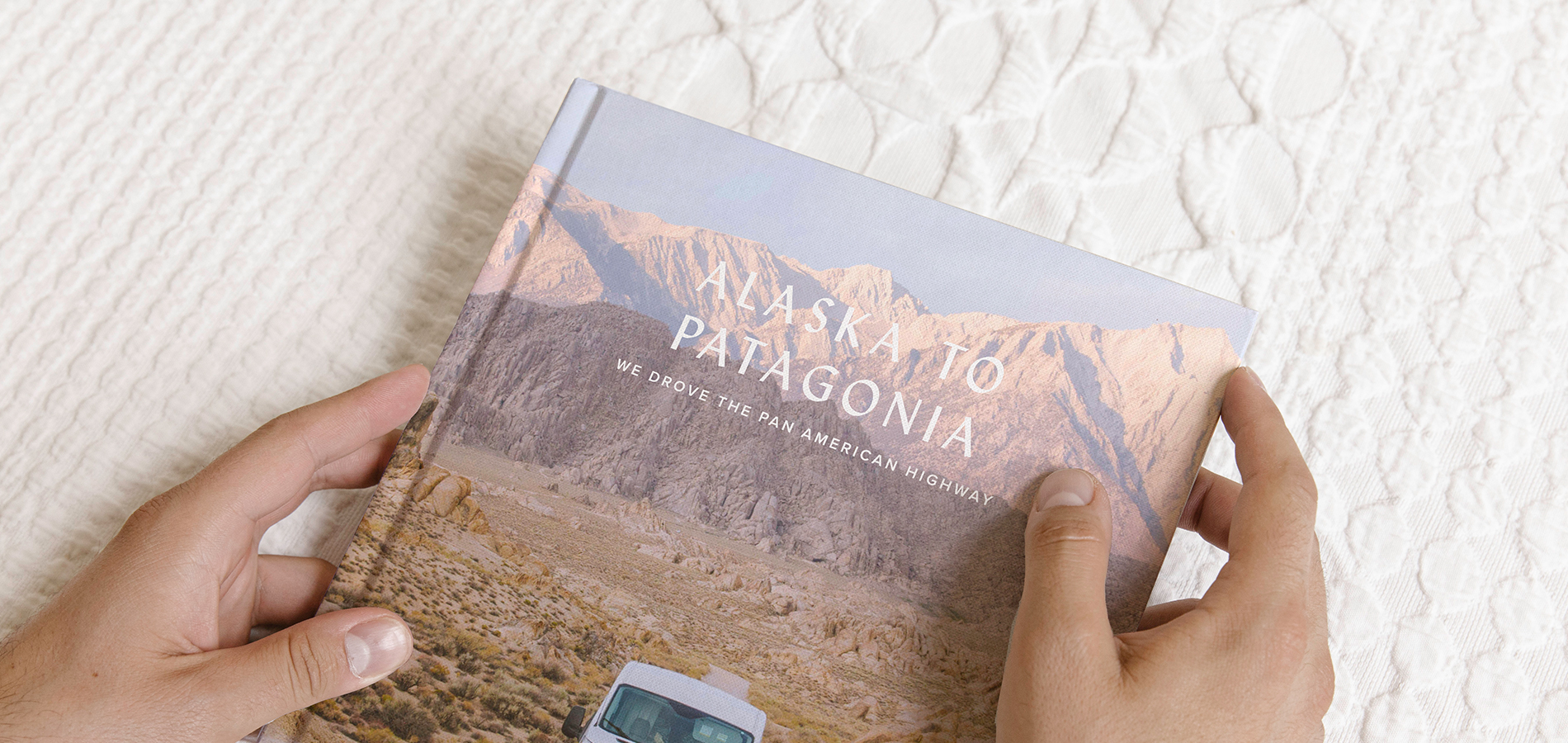 Hands holding Artifact Uprising Photo-Wrapped Hardcover Book titled Alaska to Patagonia featuring photo of camper van in front of mountainous landscape