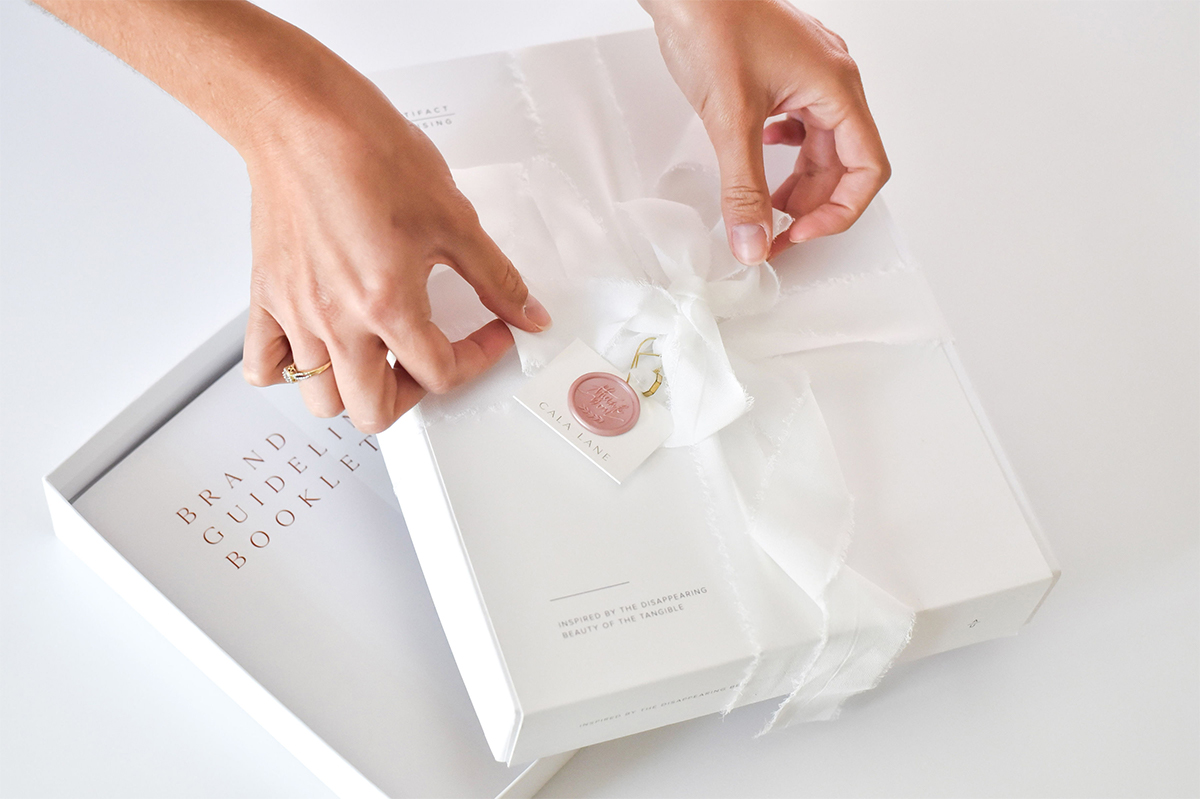 Woman's hands wrapping white bow around Artifact Uprising photo book box containing custom brand guidelines book created for a client