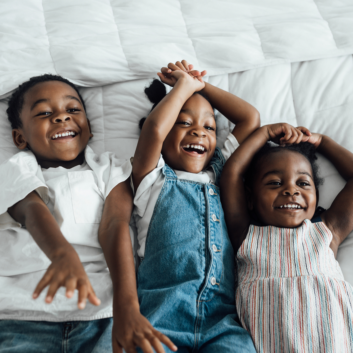 Three siblings laying in bed and laughing