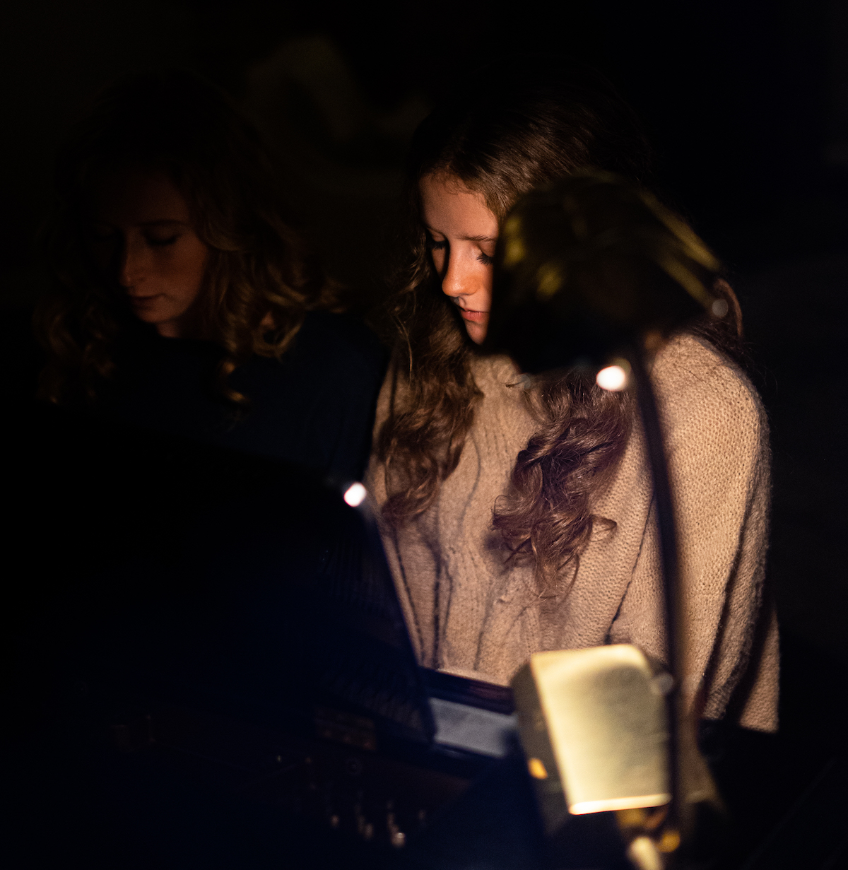 Two young women seated at the piano in the golden glow of firelight