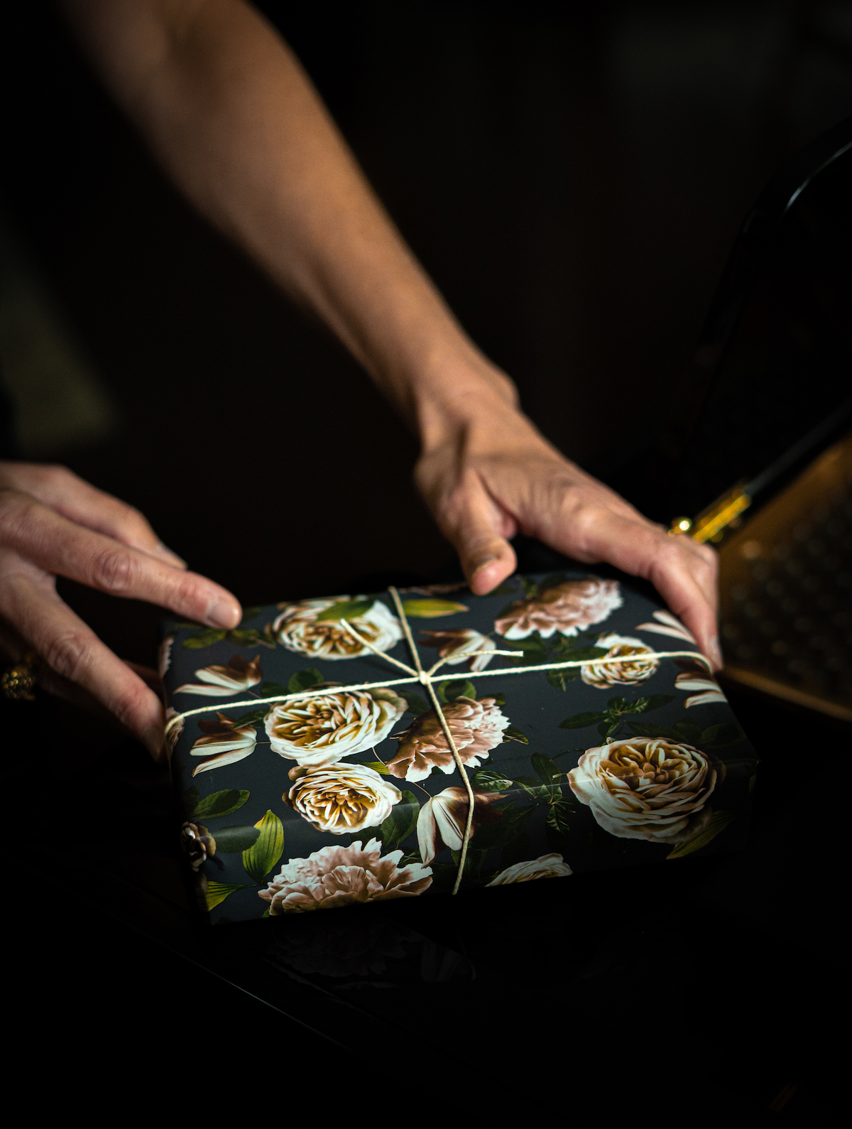 Hands setting down gift wrapped in floral wrapping paper and tied with string