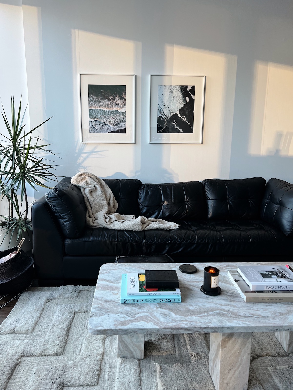 Two framed photos of the ocean by a leather couch and marbled coffee table.