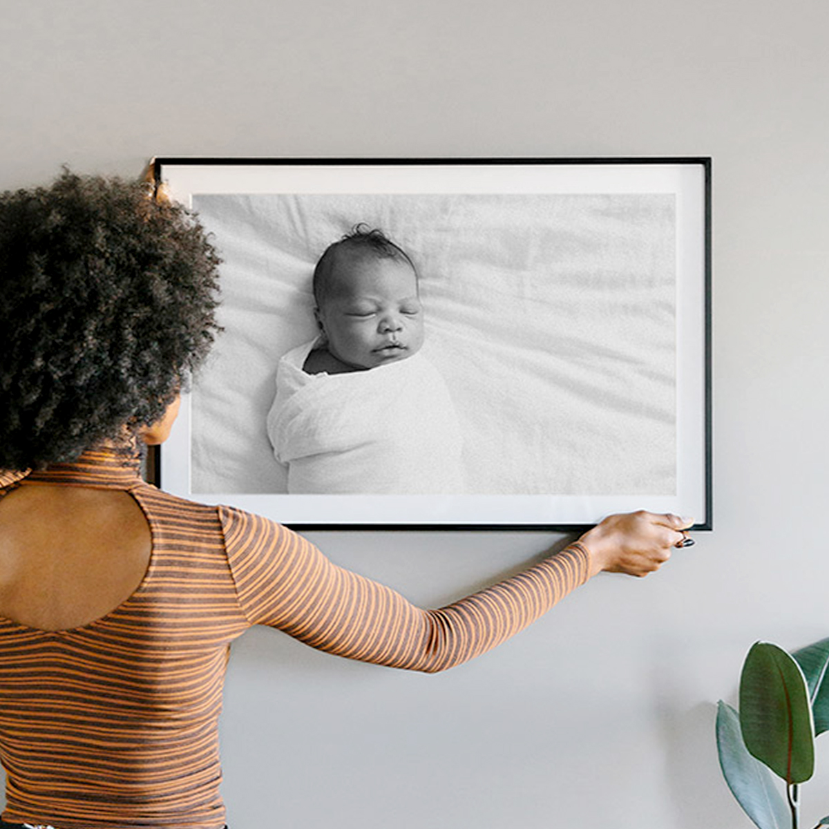 Woman hanging 20 x 30 inch Black Modern Metal Frame on the wall featuring photo of swaddled newborn matted to 16.5 x 26.5 inch
