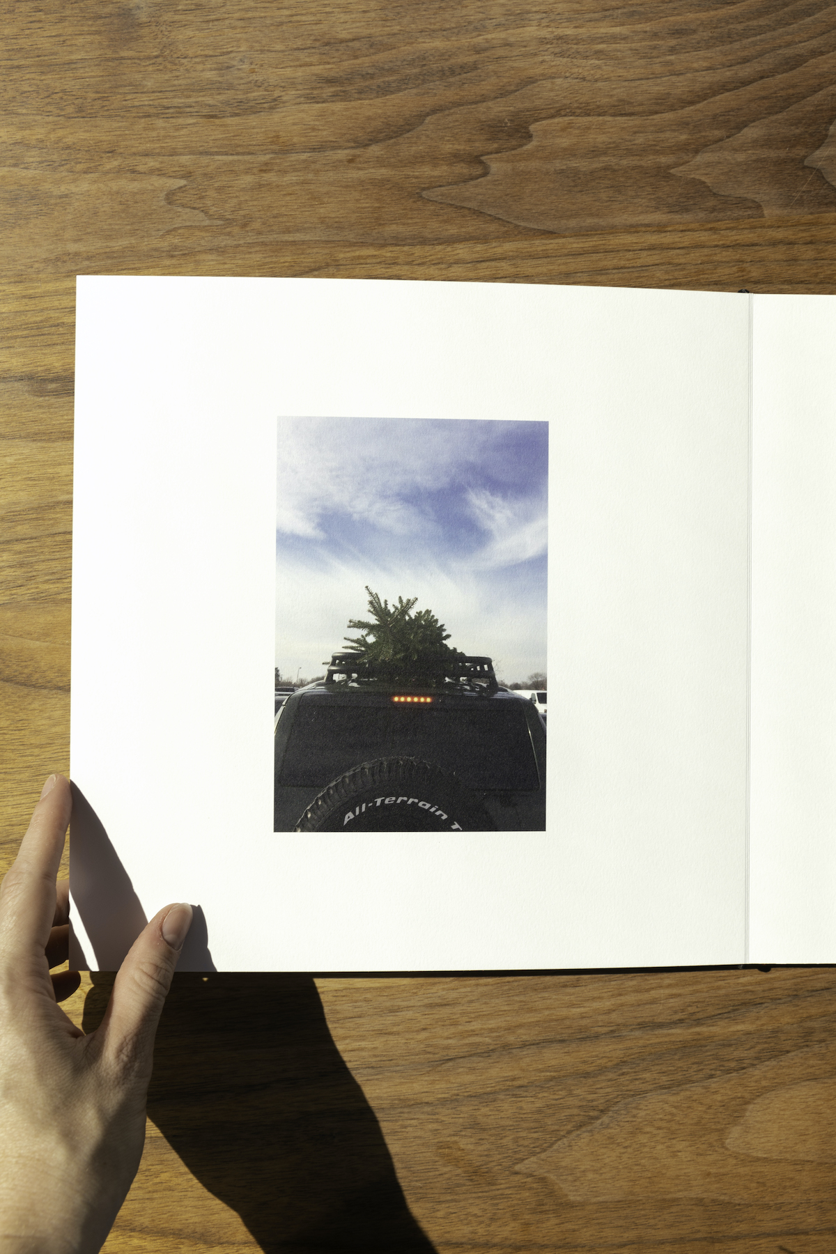 Artifact Uprising Layflat Photo Album opened to photo of pine tree strapped to the top of a Jeep