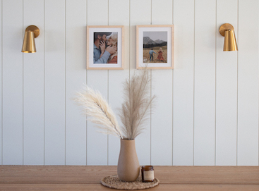 Behind a dining room table is a shiplap wall with two sconces and two Artifact Uprising Gallery Frames in maple finish. 
