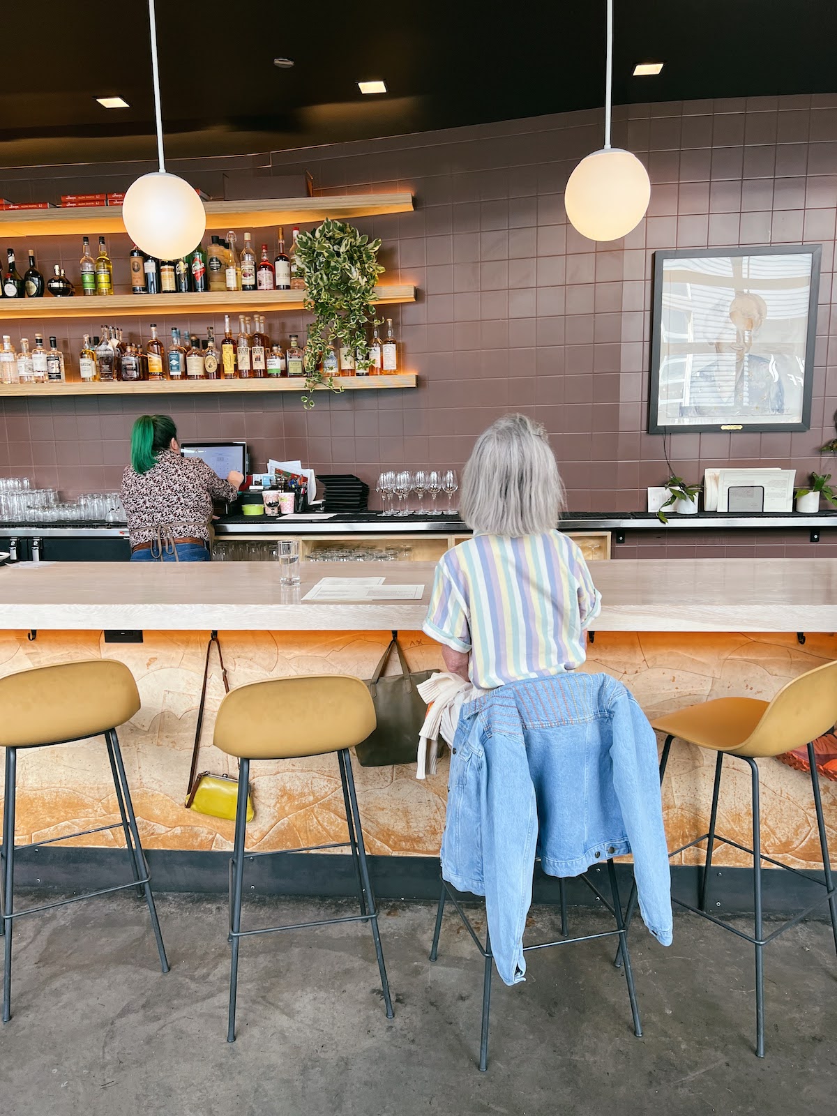 Photo taken from behind of woman sitting at the bar in a stool