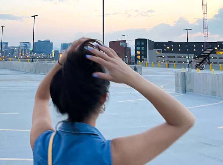 Woman holds her hair up as she gazes into the distance in an empty rooftop parking lot