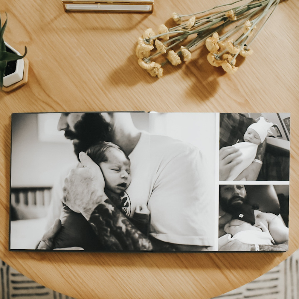 Artifact Uprising Layflat Photo Album on coffee table opened to black and white photos of father holding newborn