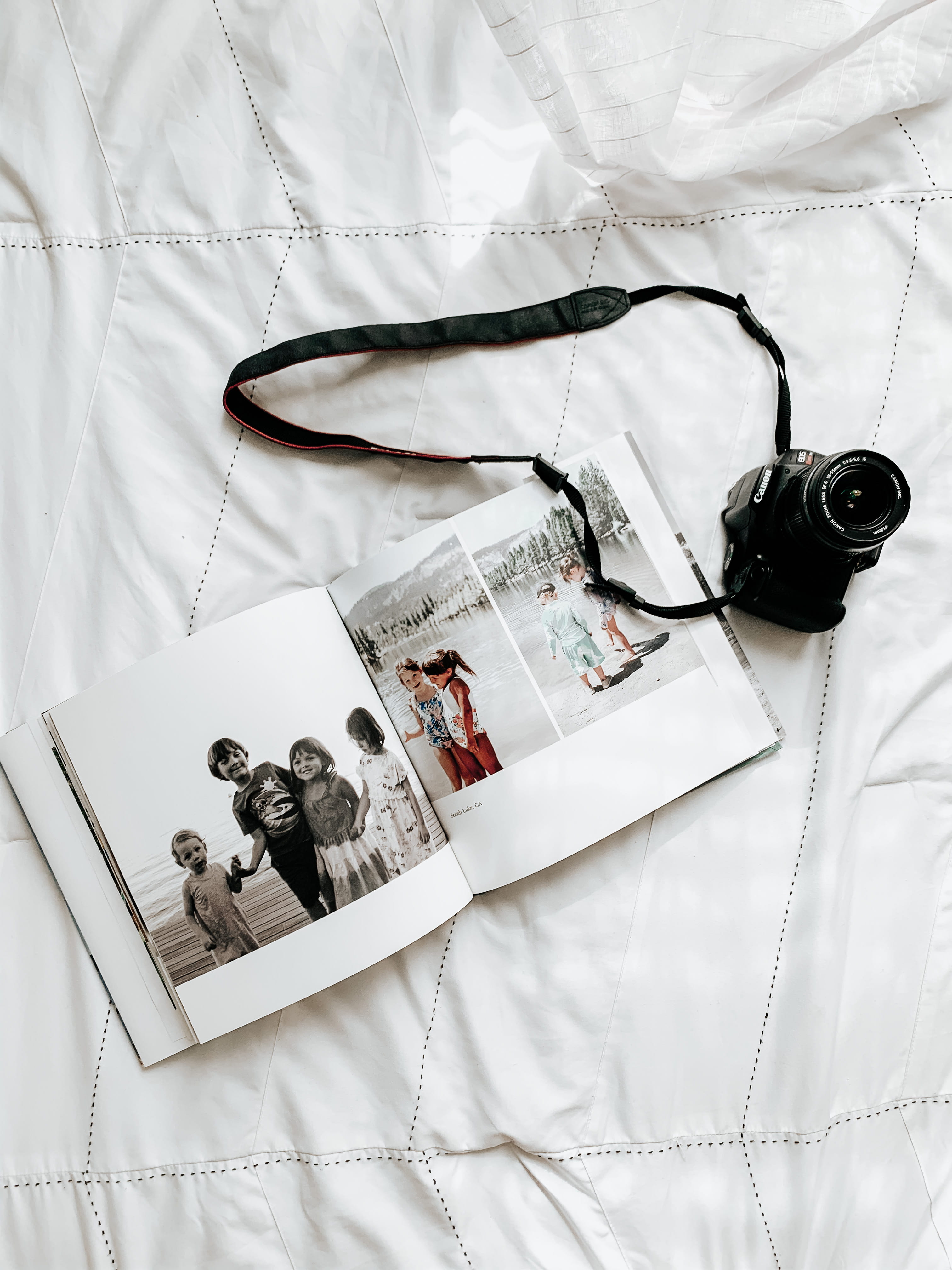 Photo book of children laughing on a bed alongside a camera. 